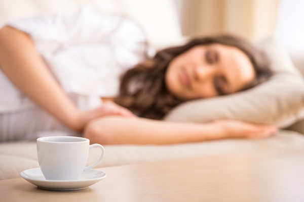 Young woman is sleeping in the bed. Focus on a cup on the table.